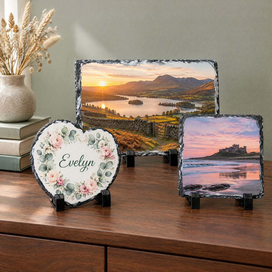 Rock photo slates: three slates showing a lake at sunset, a castle on the coast and a heart-shaped floral wreath with the name Evelyn, on a wooden shelf