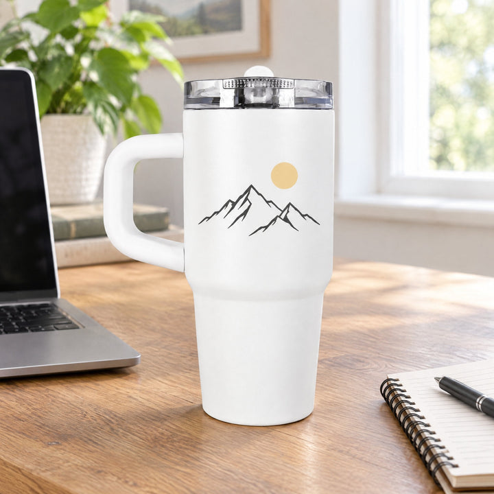 14oz sublimation tumbler printed with line-art mountains and a yellow sun, on a wooden desk beside a laptop