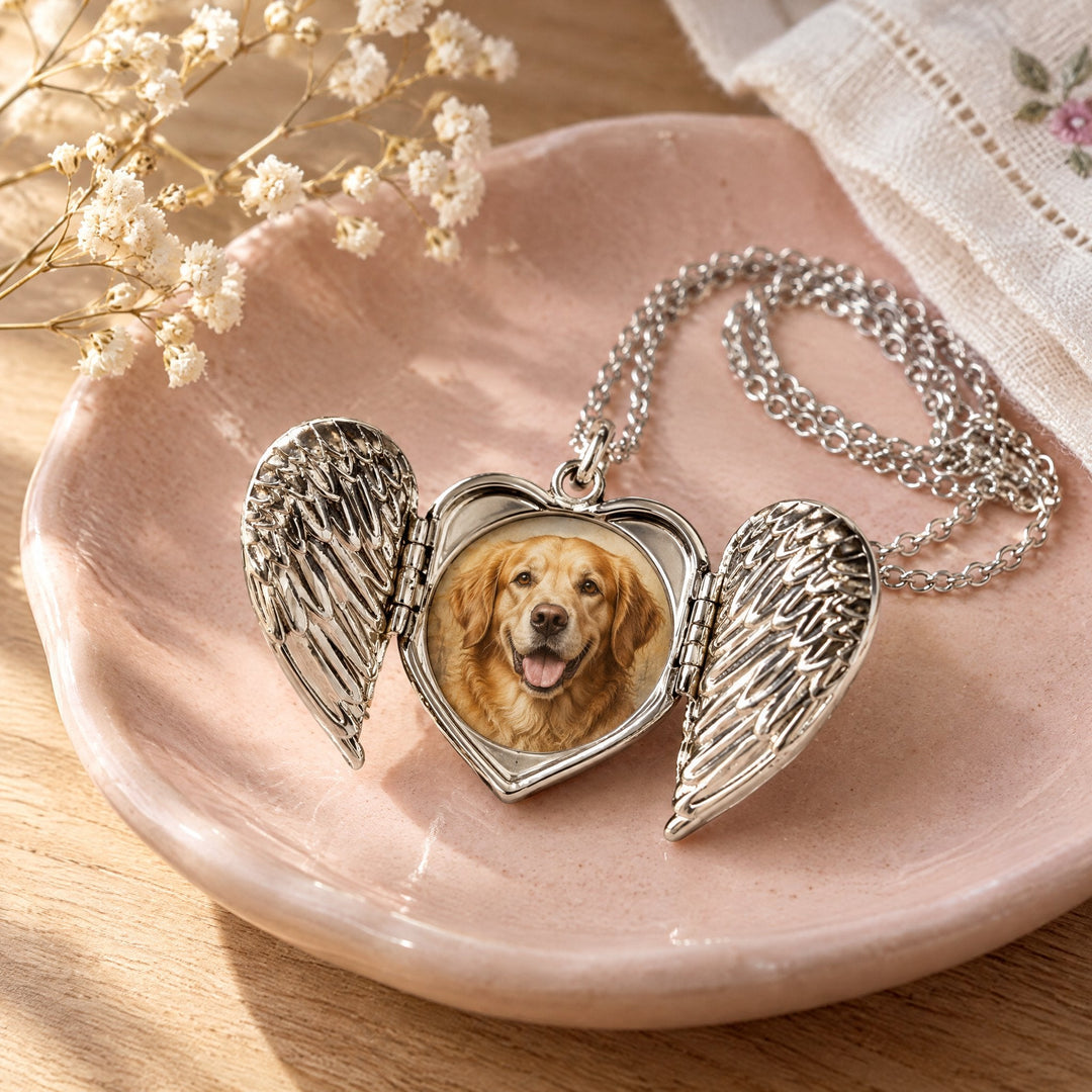 Angel wings locket printed with a golden retriever portrait, lying open on a pink ceramic jewellery dish