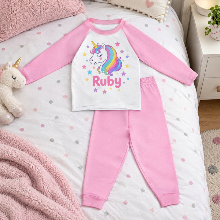 Sublimation pyjamas, pink, printed with a rainbow unicorn, stars and the name Ruby, laid out on a spotty child&