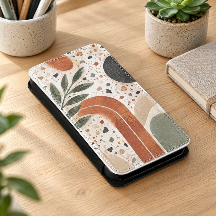 iPhone 13 Mini phone case printed with a terrazzo-and-arches abstract design, lying on a desk