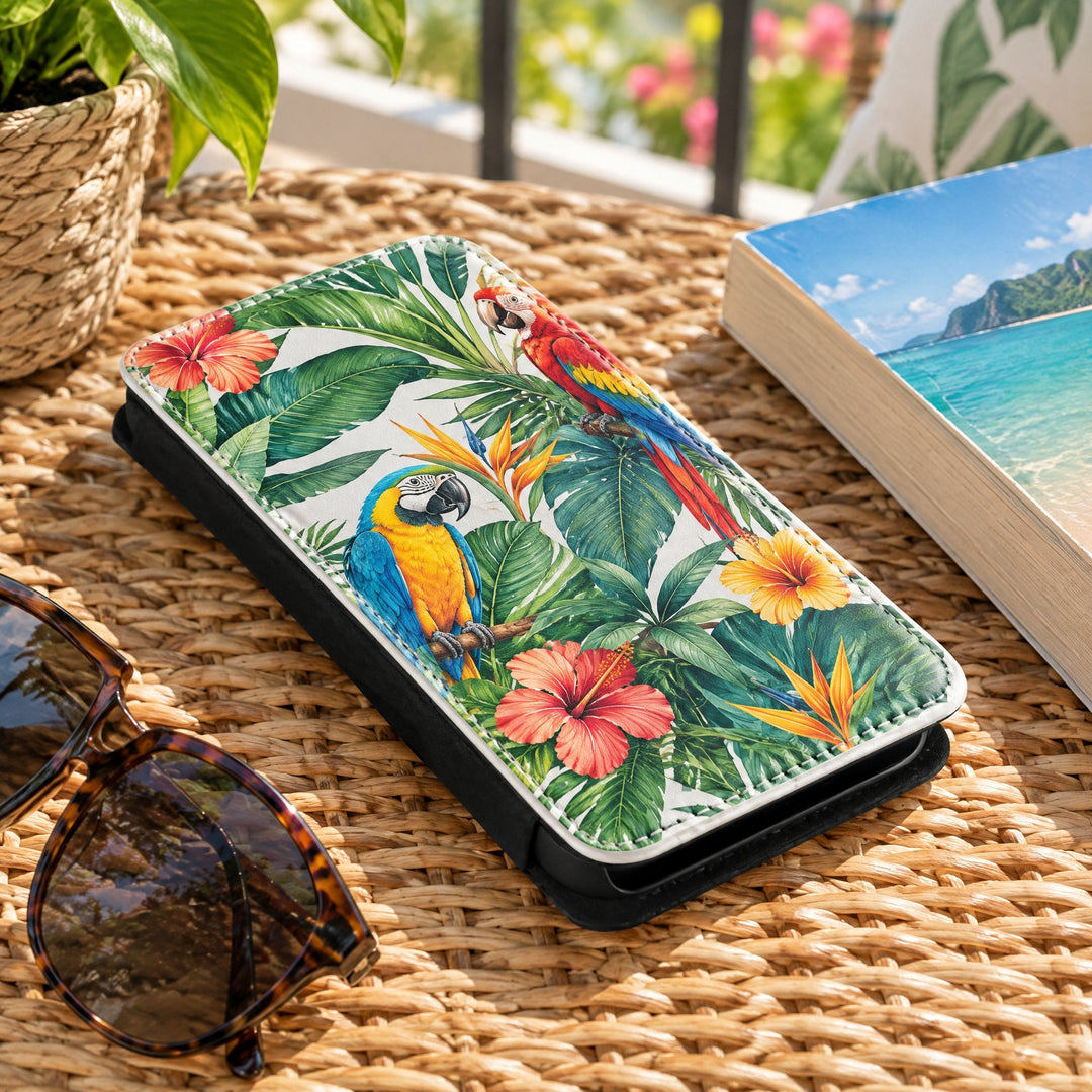 iPhone 14 phone cover printed with parrots and tropical flowers, on a woven rattan table beside sunglasses