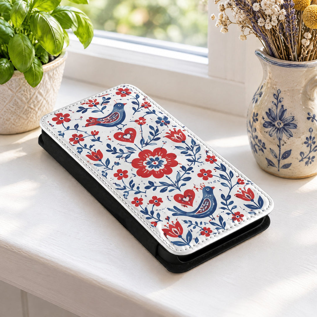 iPhone 14 Plus phone case printed with red and blue flowers, on a kitchen windowsill