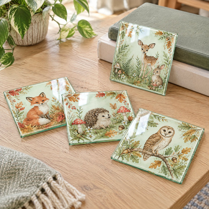 Square glass coasters printed with an illustrated woodland design, on a coffee table