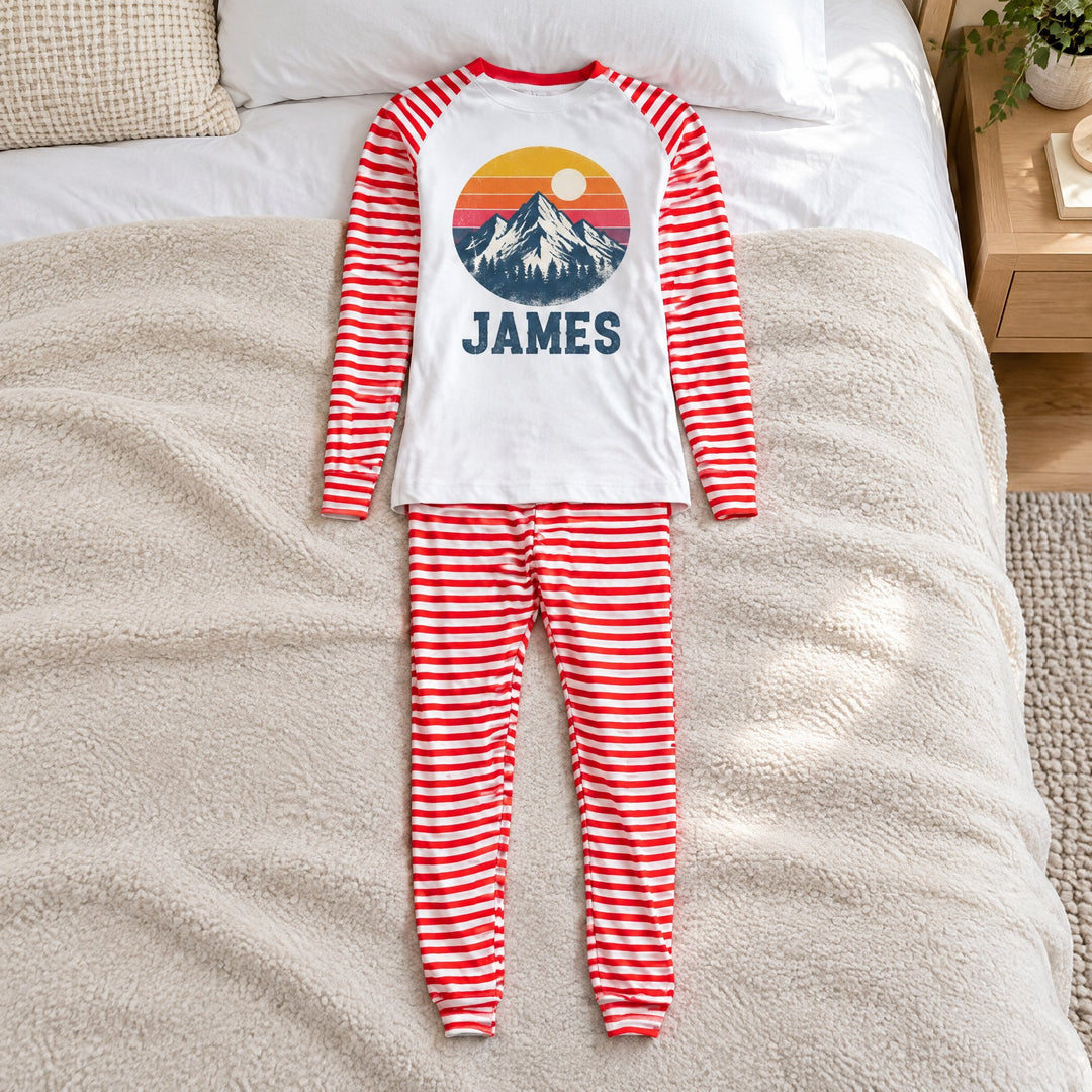 Sublimation pyjamas, mens, printed with a mountain range at sunset design and the name James, laid out on a double bed